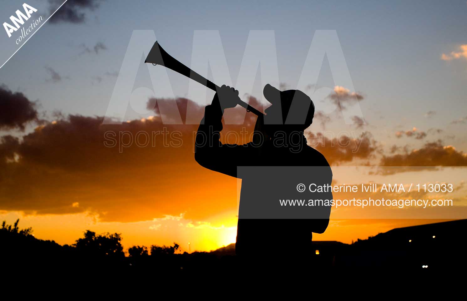 A silhouette of a football fan blowing a vuvuzela horn against the sunset